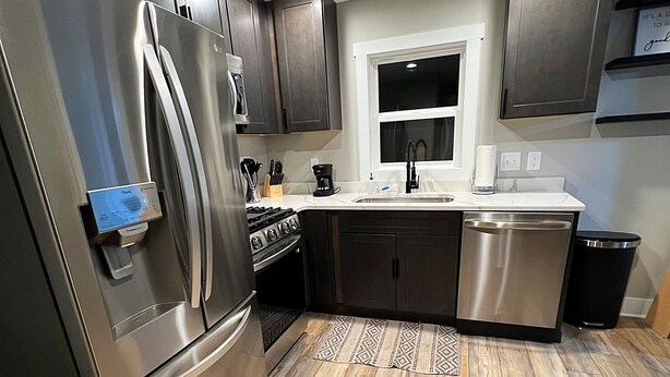 A modern kitchen with stainless steel appliances, dark cabinetry, and a wooden floor. - 3- Bedroom Bungalow 20 Minutes From ND Campus (Elkhart)