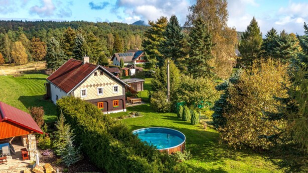 A residential area with a large house featuring a swimming pool, surrounded by lush greenery and a hilly landscape in the background.