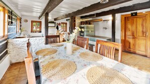 A dining area with a long table, woven placemats, wooden chairs, and a rustic ceiling.