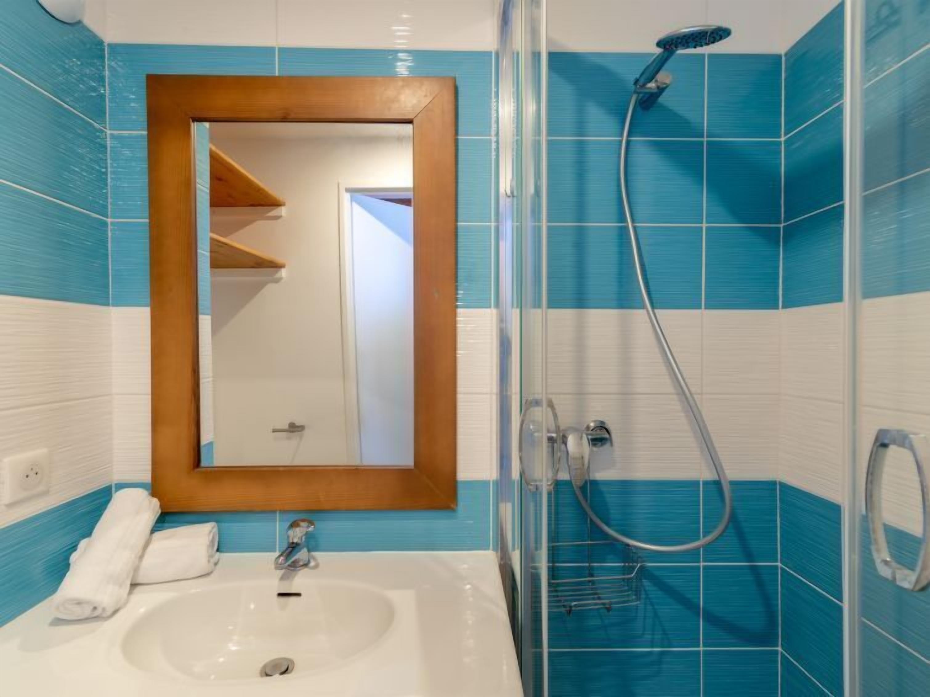 A bathroom with a white sink, a wooden-framed mirror, and a shower with a handheld showerhead.