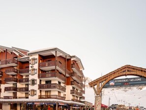 A multi-story hotel with balconies, a ski resort sign, and shops at the ground level.