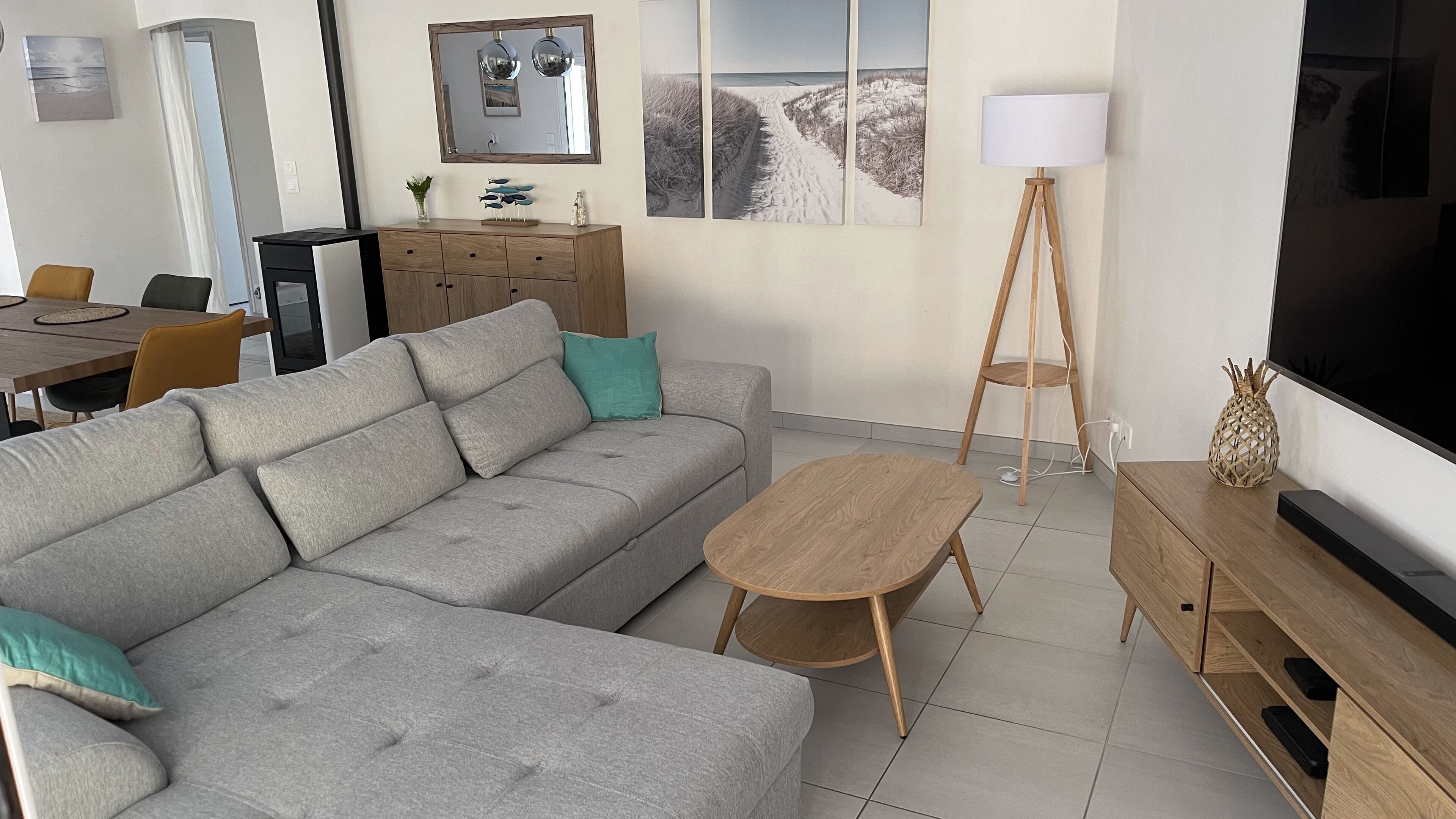 A modern living room with a grey sectional sofa, a wooden coffee table, a TV stand, and a dining area with a table and chairs.