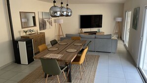 A modern living room with a dining area, grey sofa, flat-screen TV, and decorative wall art. - House 200m from the beach (La Tranche-sur-Mer)