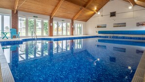 En inomhuspool med väggar av genomskinligt glas, träbjälkar i taket och en blå kakelbeklädd kant.