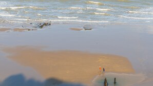 En strand med lugna vågor och några få personer som promenerar längs strandkanten.