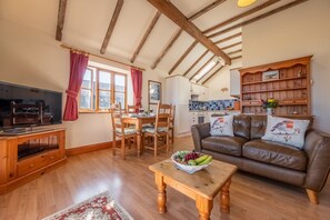 A cozy living room with a wooden TV stand, a brown leather sofa, and a dining area with wooden chairs and a table.