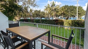 Ein Balkon mit Holztisch und -stühlen, einem weißen Geländer und Blick auf eine angelegte Grünfläche mit Bäumen und einem Gewässer.