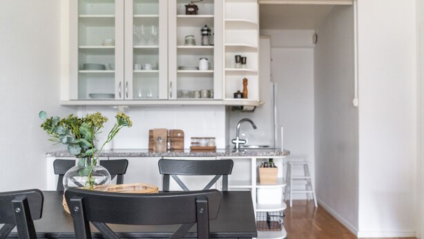 Uma cozinha moderna com armários brancos, uma mesa de jantar com cadeiras e um vaso com flores sobre a mesa.