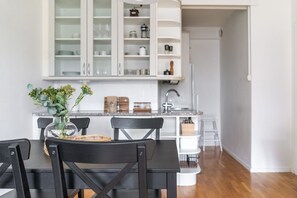 A modern kitchen with white cabinetry, a dining table with chairs, and a vase with flowers on the table. - 1br apartment with patio in Lauttasaari (Helsinki)