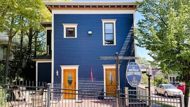 Un edificio de dos pisos con fachada azul, dos puertas de madera y un letrero que indica que es la Bayfield Guest House.