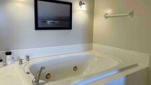 Un baño con una bañera grande, un cuadro enmarcado con barcos de vela en la pared y dos apliques.