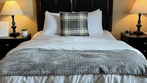 Una cama bien hecha con un almohadón escocés, dos mesitas de noche con lámparas y un aplique en la pared.