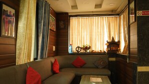 A cozy room with a sofa, a small table, and a window with curtains. - Hotel J. Palace (New Delhi)