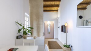 A narrow hallway with a white wall, a ceiling with wooden beams, a potted plant, a TV mounted on the wall, and a small table with a chair. - PENTHOUSE WITH SEAVIEW TERRACE IN THE CITY'S HEART (Cagliari)