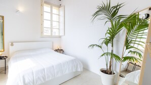 A bedroom with a large bed, a potted plant, a bedside table, and a window with open shutters. - PENTHOUSE WITH SEAVIEW TERRACE IN THE CITY'S HEART (Cagliari)