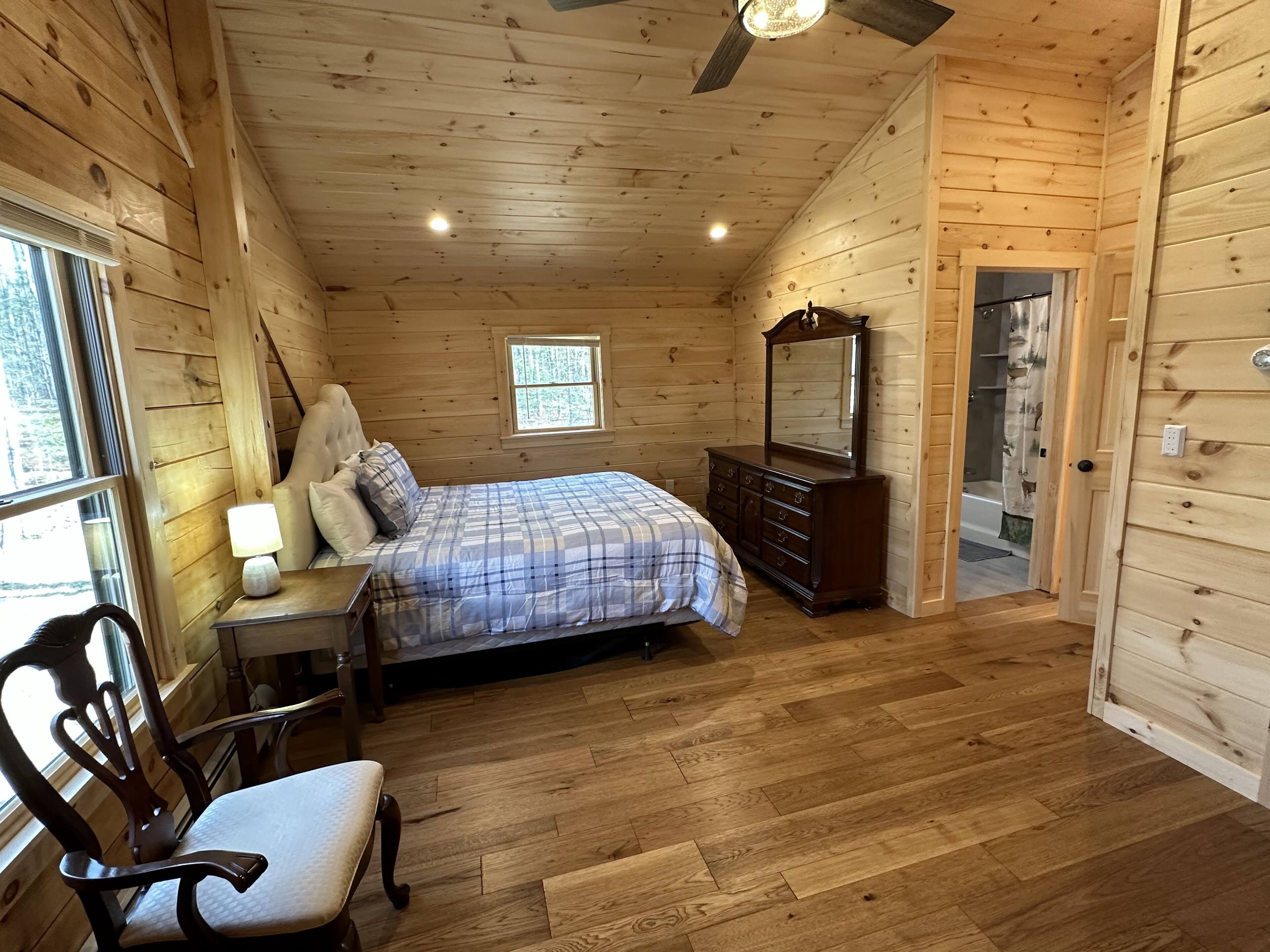 Une chambre dans une cabane en bois, avec un lit, une commode, une chaise et une petite fenêtre.