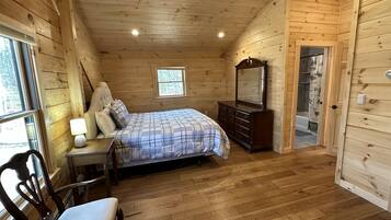 Une chambre dans une cabane en bois, avec un lit, une commode, une chaise et une petite fenêtre.