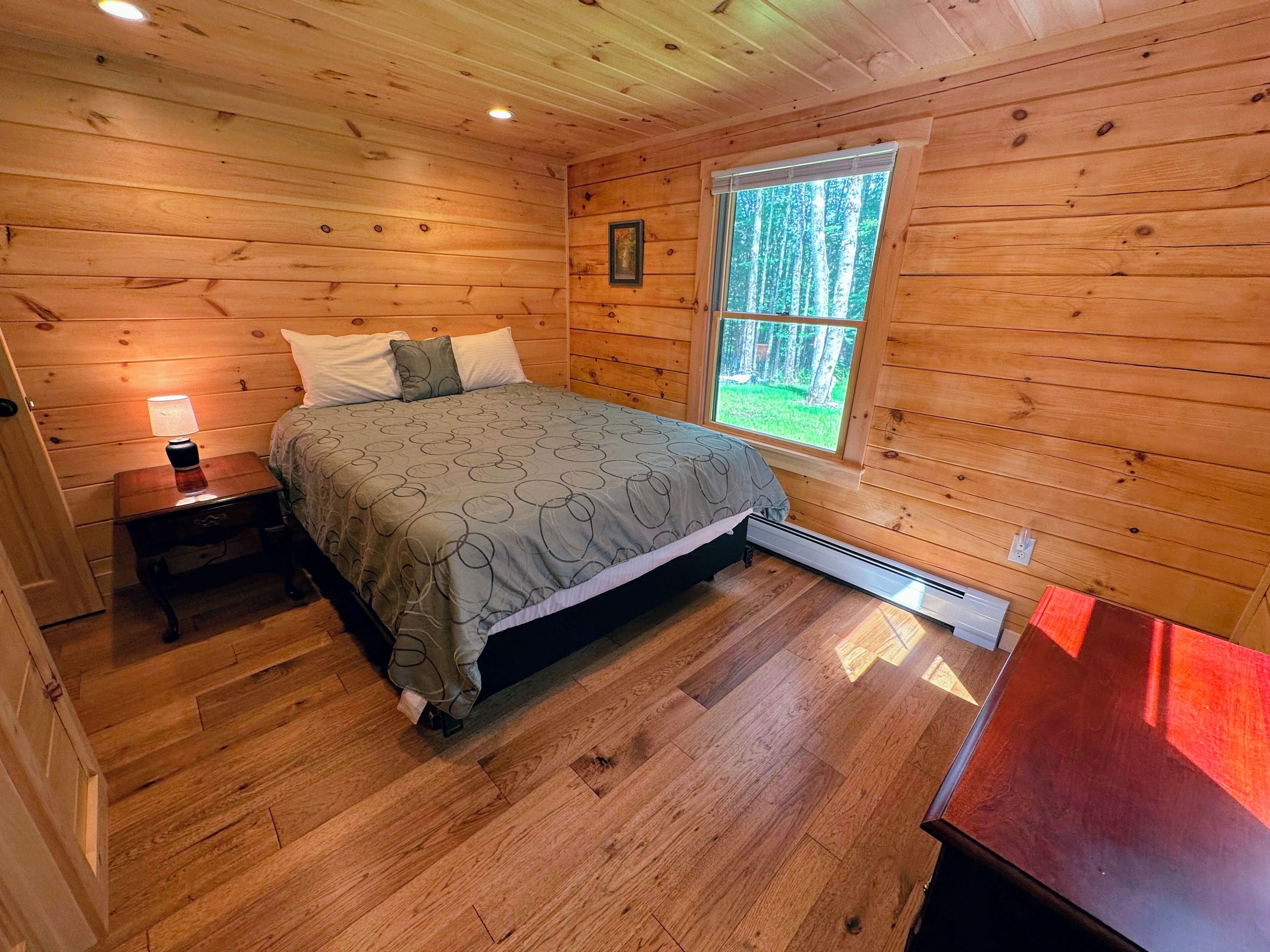 A wooden cabin bedroom with a bed, nightstand, and window.