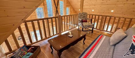 Interior acogedor de una cabaña con terraza de madera, un sofá cómodo, una mesa de madera y una silla.