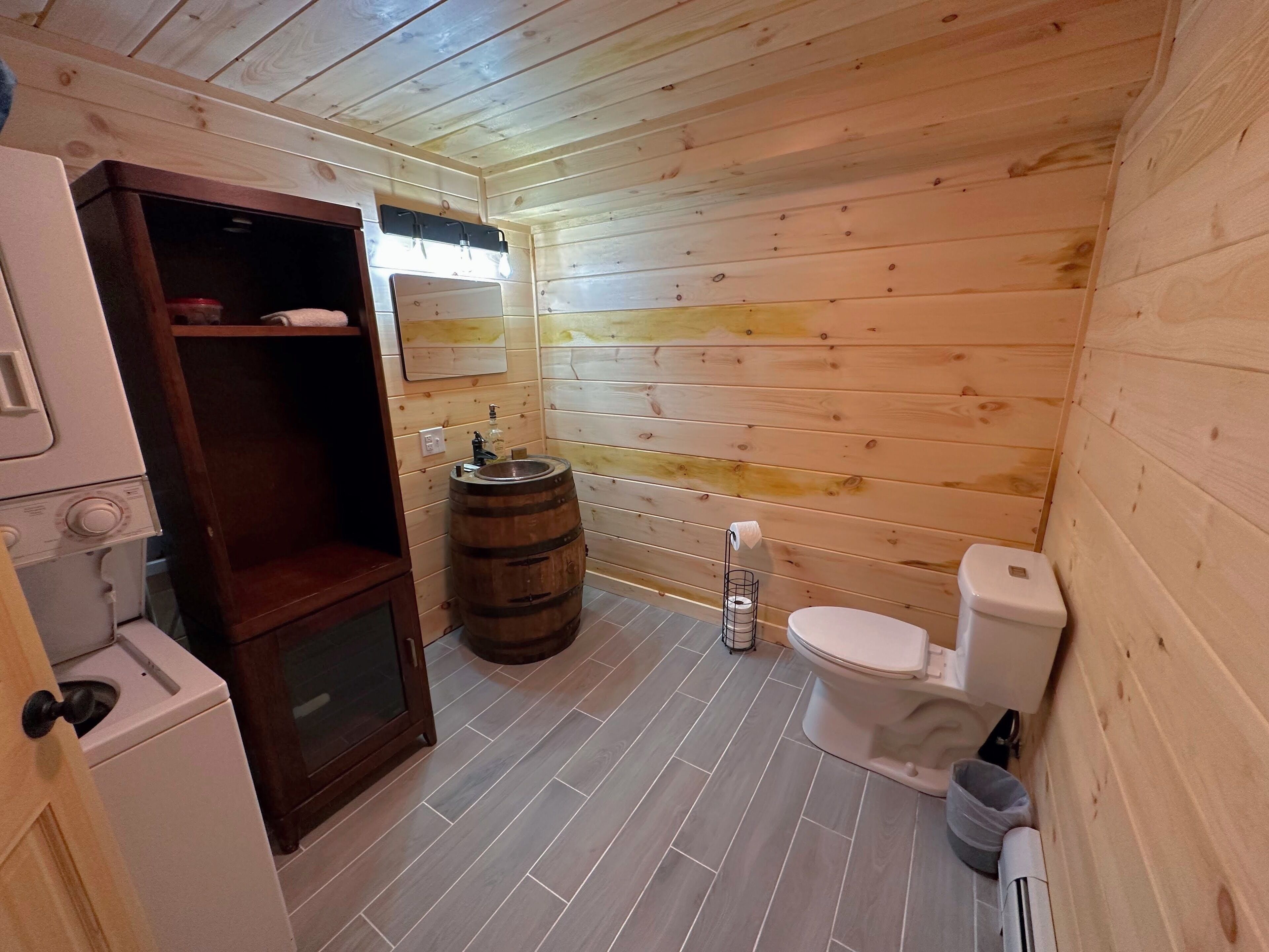 A compact wooden bathroom with a toilet, a wooden barrel, and a small shelf.