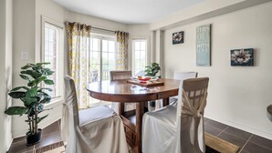 Comedor con una mesa redonda, cuatro sillas, una planta en maceta y una ventana con cortinas.