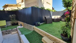 Un jardin avec une pelouse artificielle, une clôture noire, une terrasse en bois et du mobilier d’extérieur.