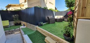 Een achtertuin met kunstgras, een zwarte omheining, een houten terras en tuinmeubilair.