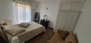 Een slaapkamer met een bed, een dressoir, een spiegel, een nachtkastje, een lamp en een garderobe.