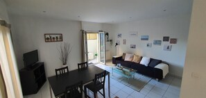 Een woonkamer met een zwarte bank, een glazen salontafel, een eettafel met stoelen, een televisie op een standaard en een schuifdeur naar een balkon.