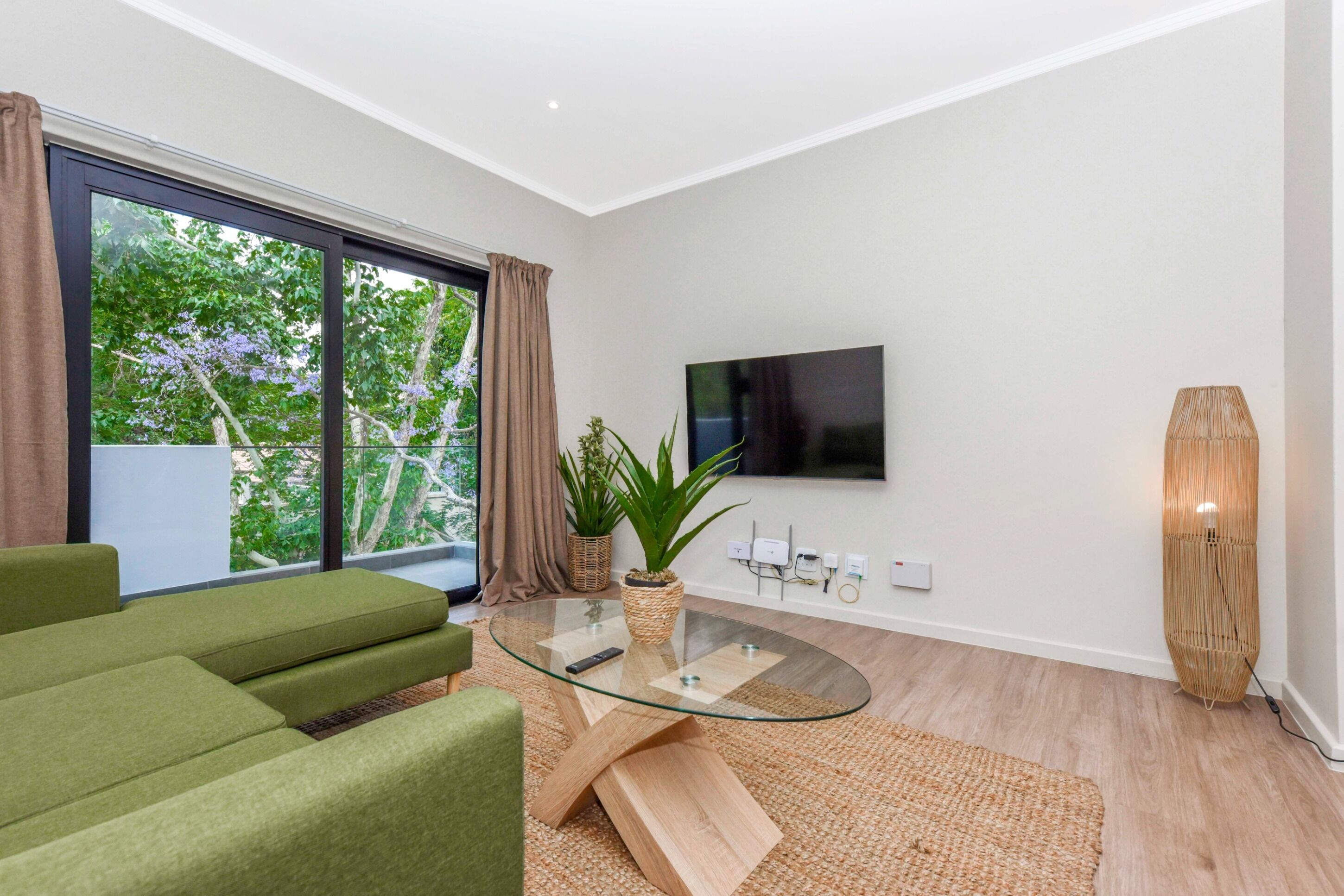 A modern living room with a glass coffee table, green sofa, and a large window with curtains.
