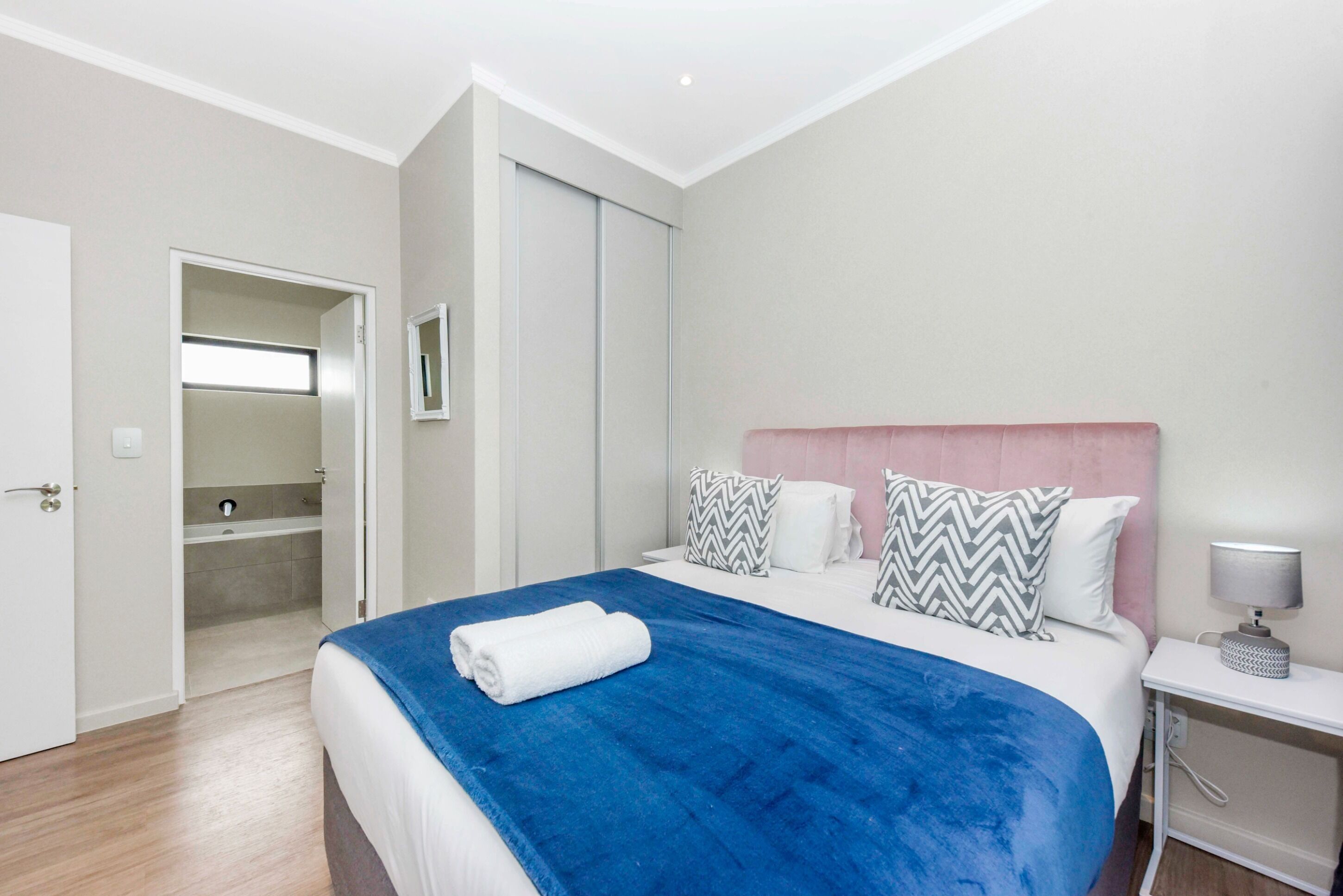 Habitación de hotel con cama, mesita de noche y baño visible a través de una puerta abierta.