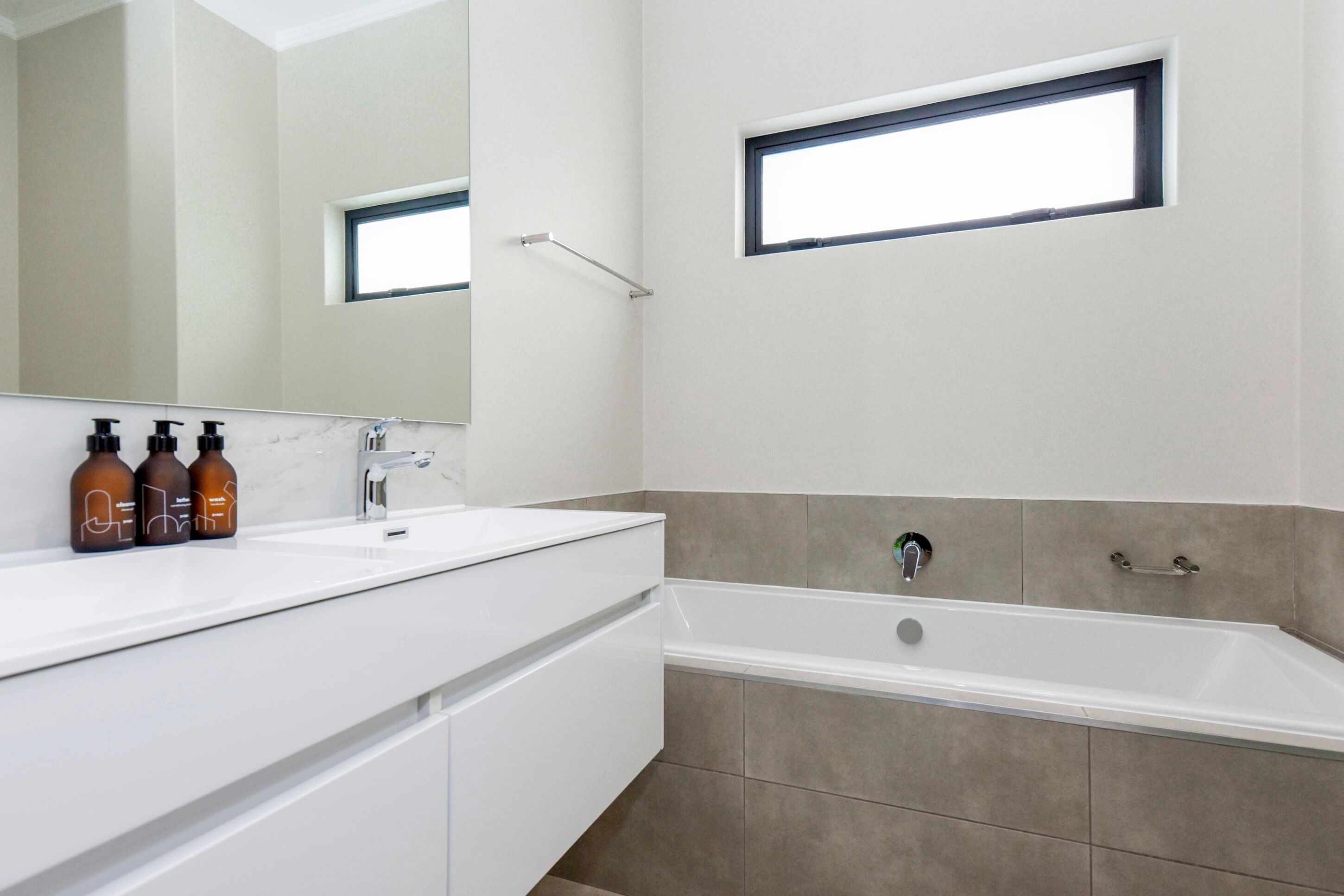 Un baño moderno con un espejo grande, dos lavamanos, una bañera y una ventana.