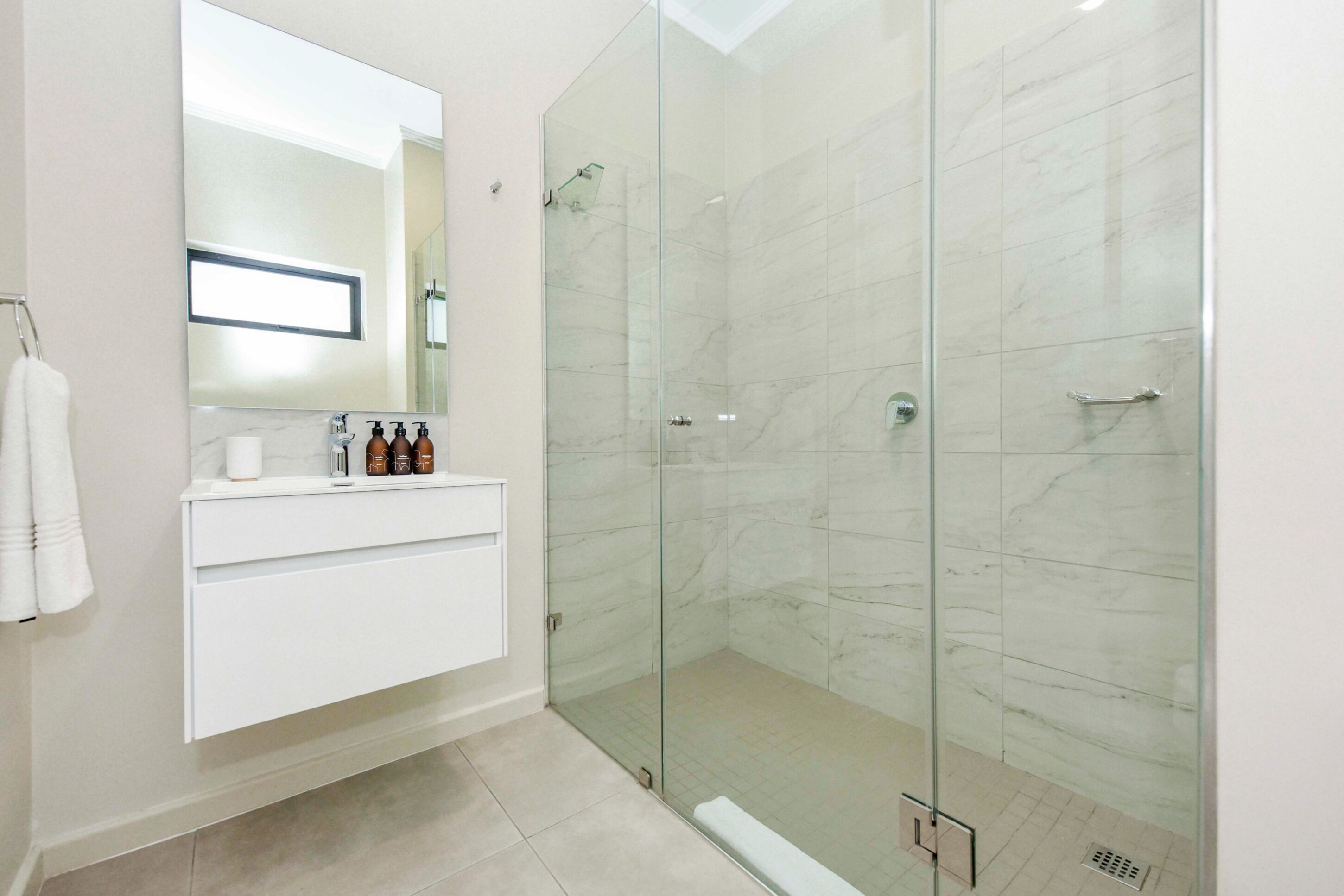 Une salle de bain moderne avec une douche à parois de verre, un meuble-lavabo blanc avec des articles de toilette et un grand miroir.