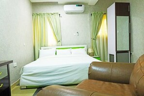 Habitación de hotel con una cama, un sillón de cuero marrón, un armario y un equipo de aire acondicionado.