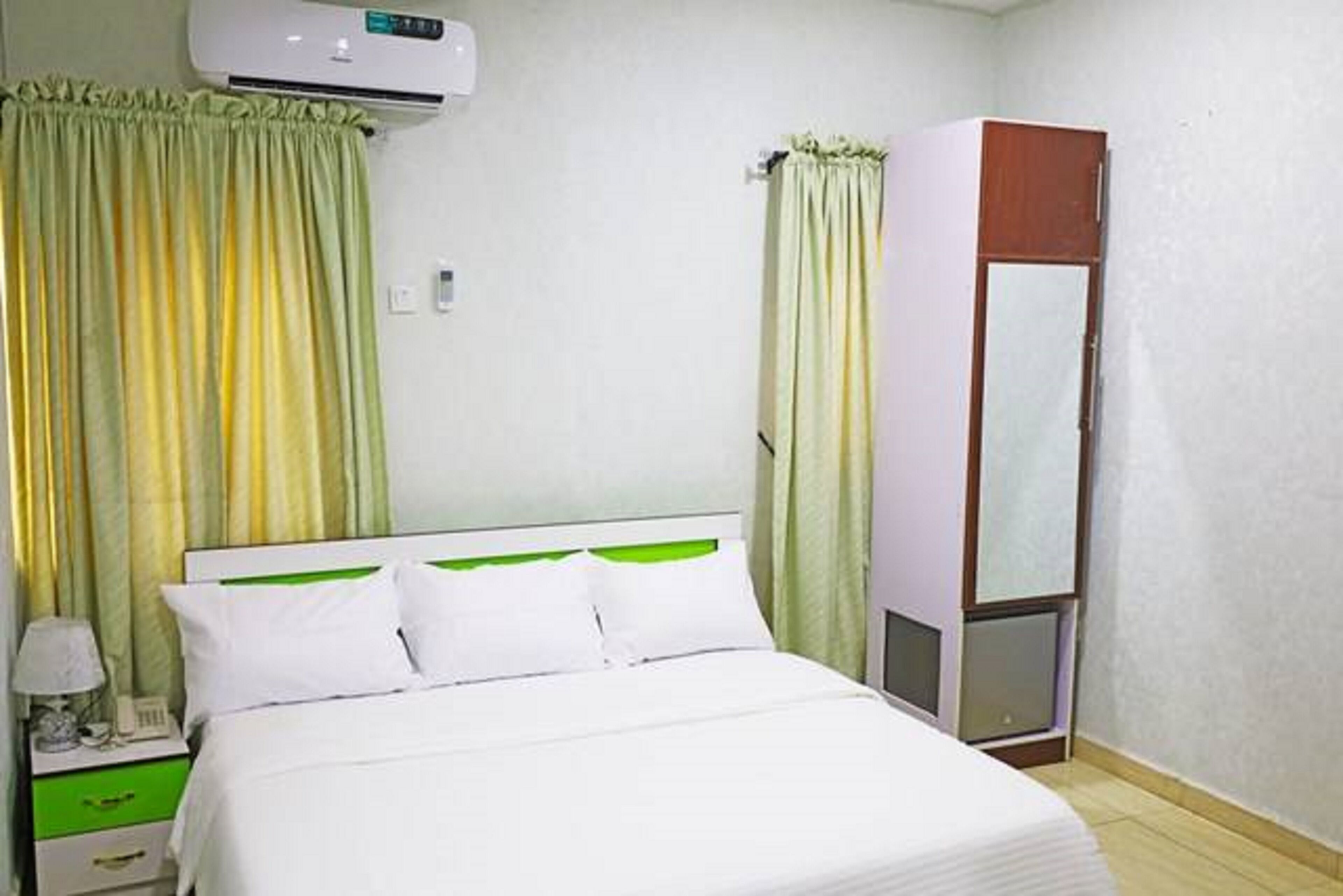 A hotel room with a bed, a nightstand, a wardrobe, and an air conditioning unit.
