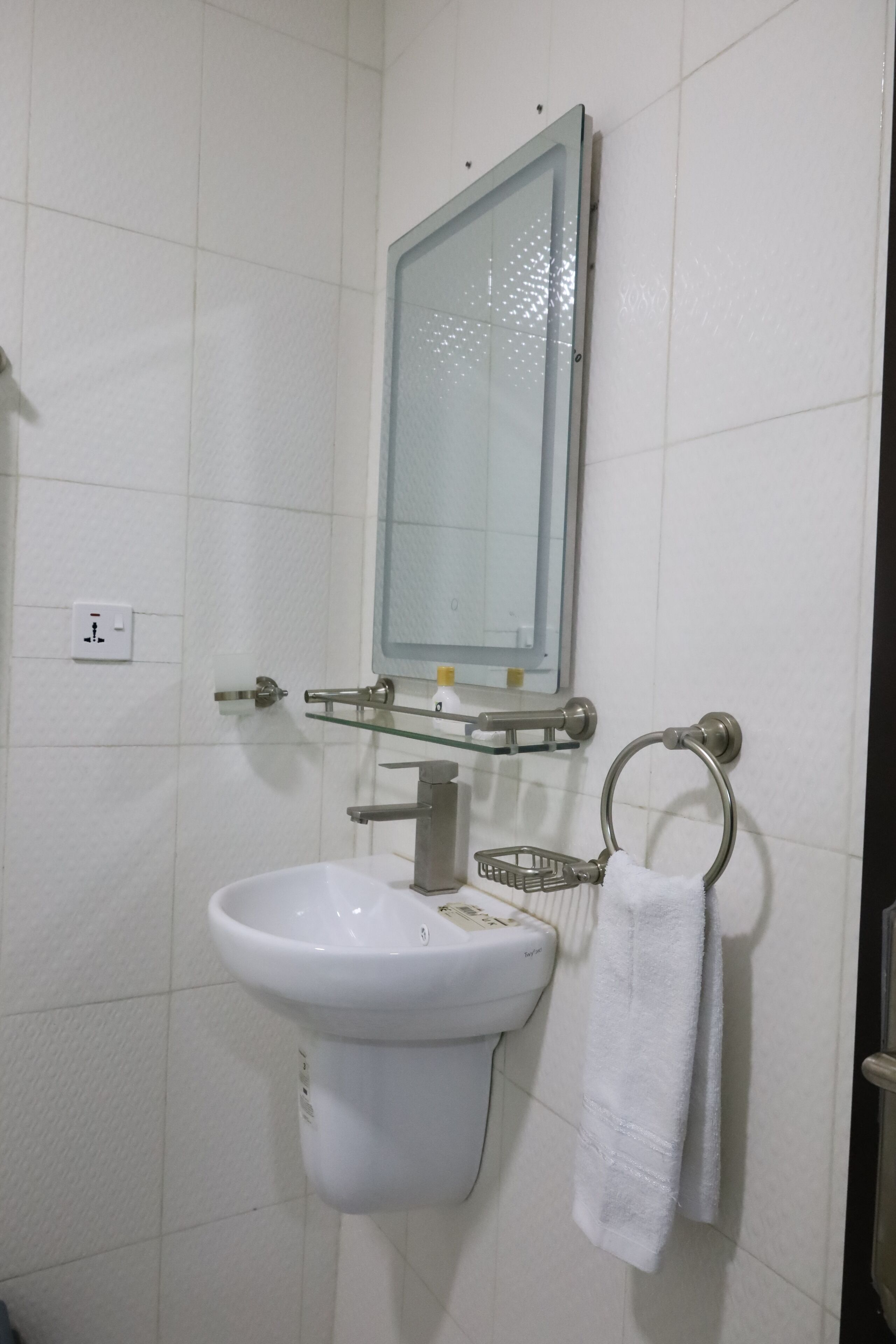 Un baño con un lavamanos blanco, un espejo y un perchero para toallas.