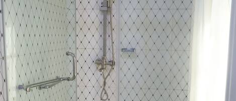Un área de ducha con paredes de vidrio, suelo de baldosas, cabezal de ducha y barra de apoyo.