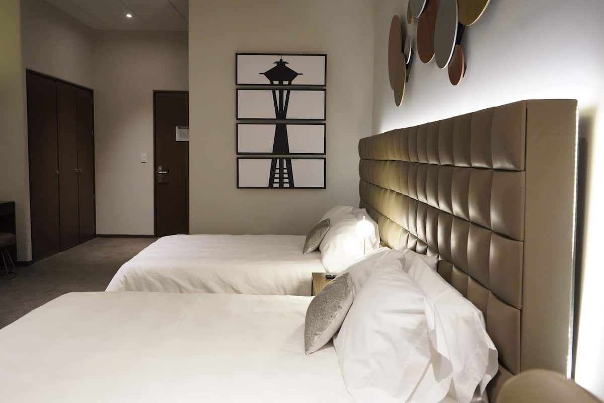 Une chambre d’hôtel avec deux lits, une tête de lit, une œuvre d’art murale et une porte.