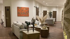 A modern hotel lobby with a wooden floor, a white sofa, a coffee table with decorative plants, and a large abstract painting on the wall. - Antigua Hotel Boutique (Atizapan de Zaragoza)