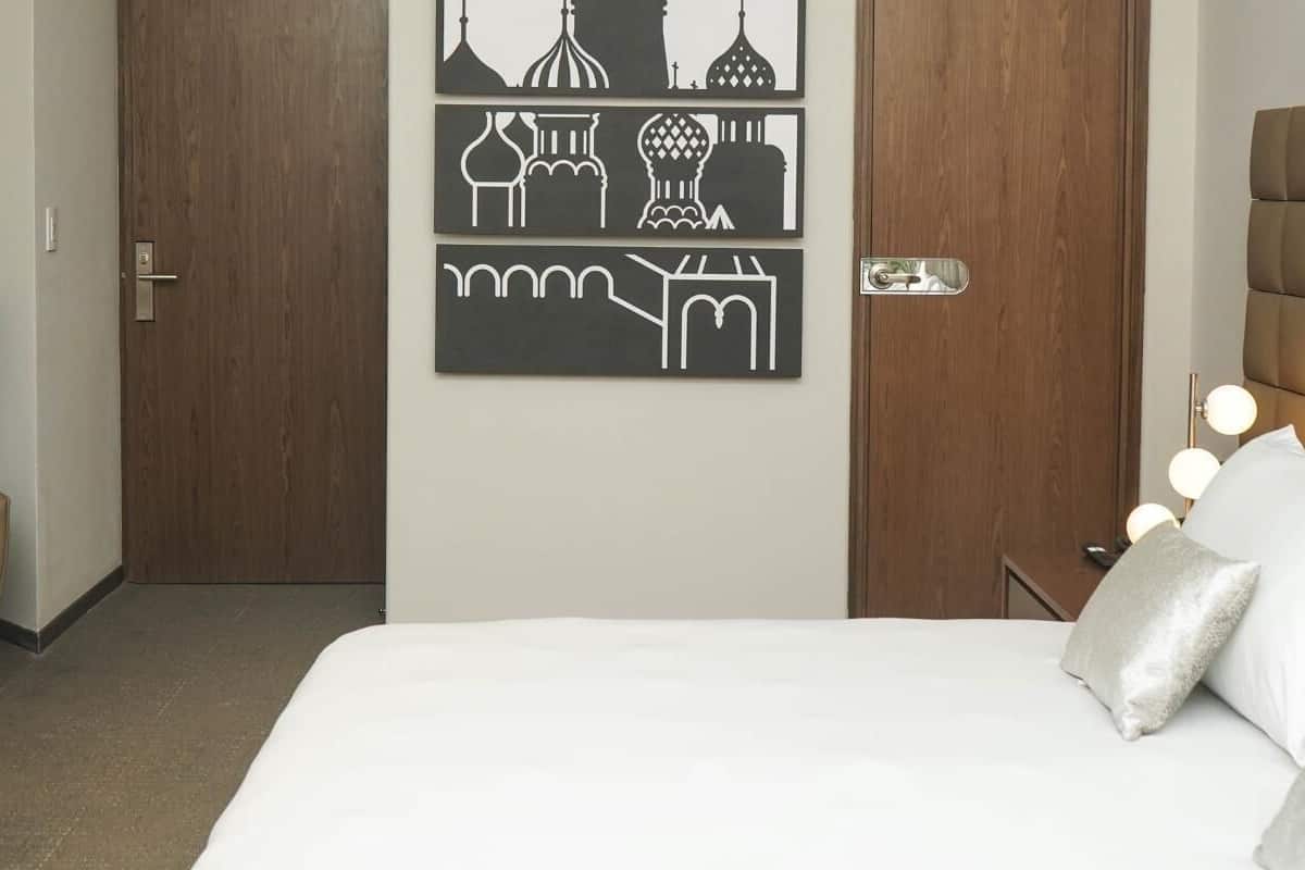 Une chambre d’hôtel avec un lit, une chaise, un bureau et un mur décoré d’œuvres d’art.