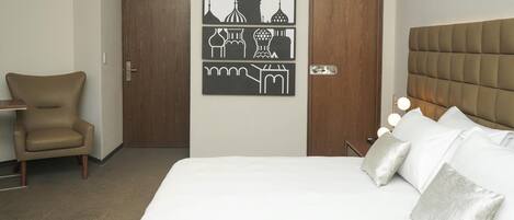 Ein Hotelzimmer mit einem Bett, einem Sessel, einem Schreibtisch und einer Wand mit Kunstwerken.