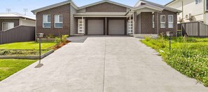 A two-story brick house with a garage, a front lawn, and a clear sky. - Libbity's at The Point by Experience Jervis Bay (Sanctuary Point)