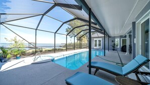 Piscina techada al aire libre con sillones de descanso, vista al océano y puerta de vidrio que da al interior.