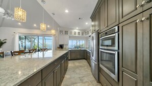 Una cocina moderna con armarios oscuros, electrodomésticos de acero inoxidable e iluminación colgante.