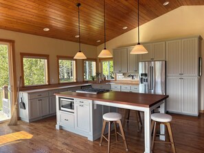 A spacious kitchen with wooden flooring, a large island, and pendant lighting. - Large Bigfork Home, summer availability! Mountain Views-Family friendly! (Bigfork)