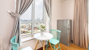 A small room with a window, a table with chairs, a refrigerator, and a vase with flowers. - The Manor  Apartment Nguyen Huu Canh (Ho Chi Minh City)