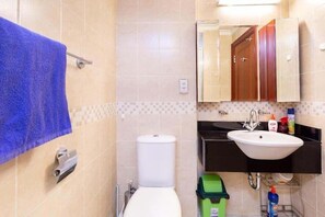 Une salle de bain avec des toilettes blanches, un lavabo et un miroir. Une serviette bleue est suspendue à un porte-serviettes.