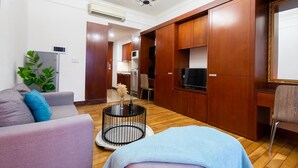 A modern living room with a sofa, a round coffee table, and a TV. There is a wooden cabinet and a chair. - The Manor  Apartment Nguyen Huu Canh (Ho Chi Minh City)