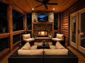 A cozy room with a stone fireplace, two sofas, a television, and a ceiling fan.