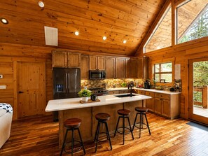 A wooden cabin interior with a kitchen featuring a refrigerator, microwave, and bar stools.